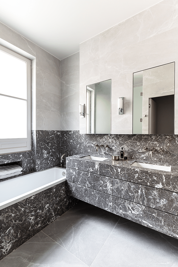 Salle de bains en marbre gris avec baignoire encastrée, plan-vasque monolithique et grand miroir