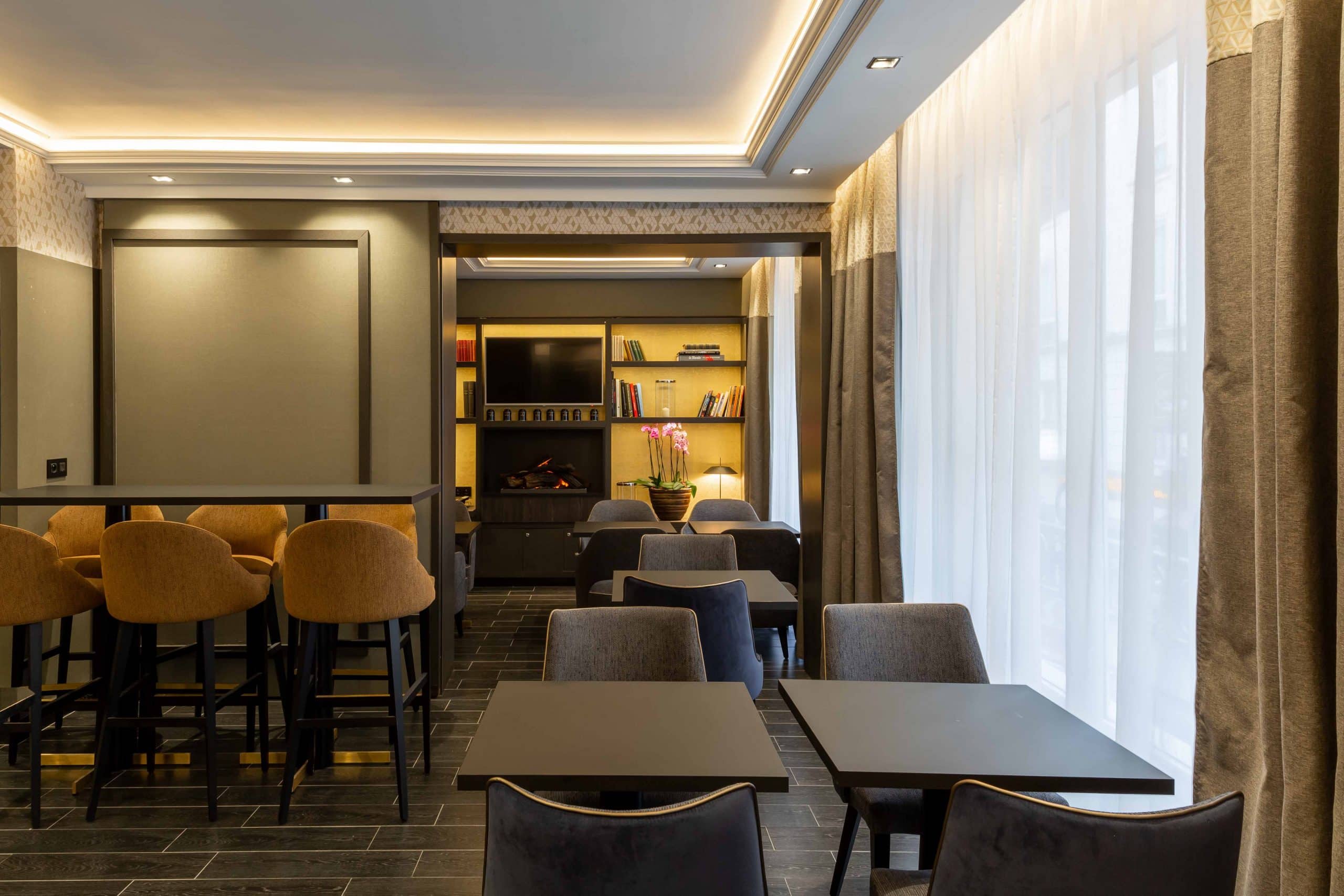 Espace commun de l'Hôtel Daunou Opéra, comptoir bar et tables devant de grandes fenêtres
