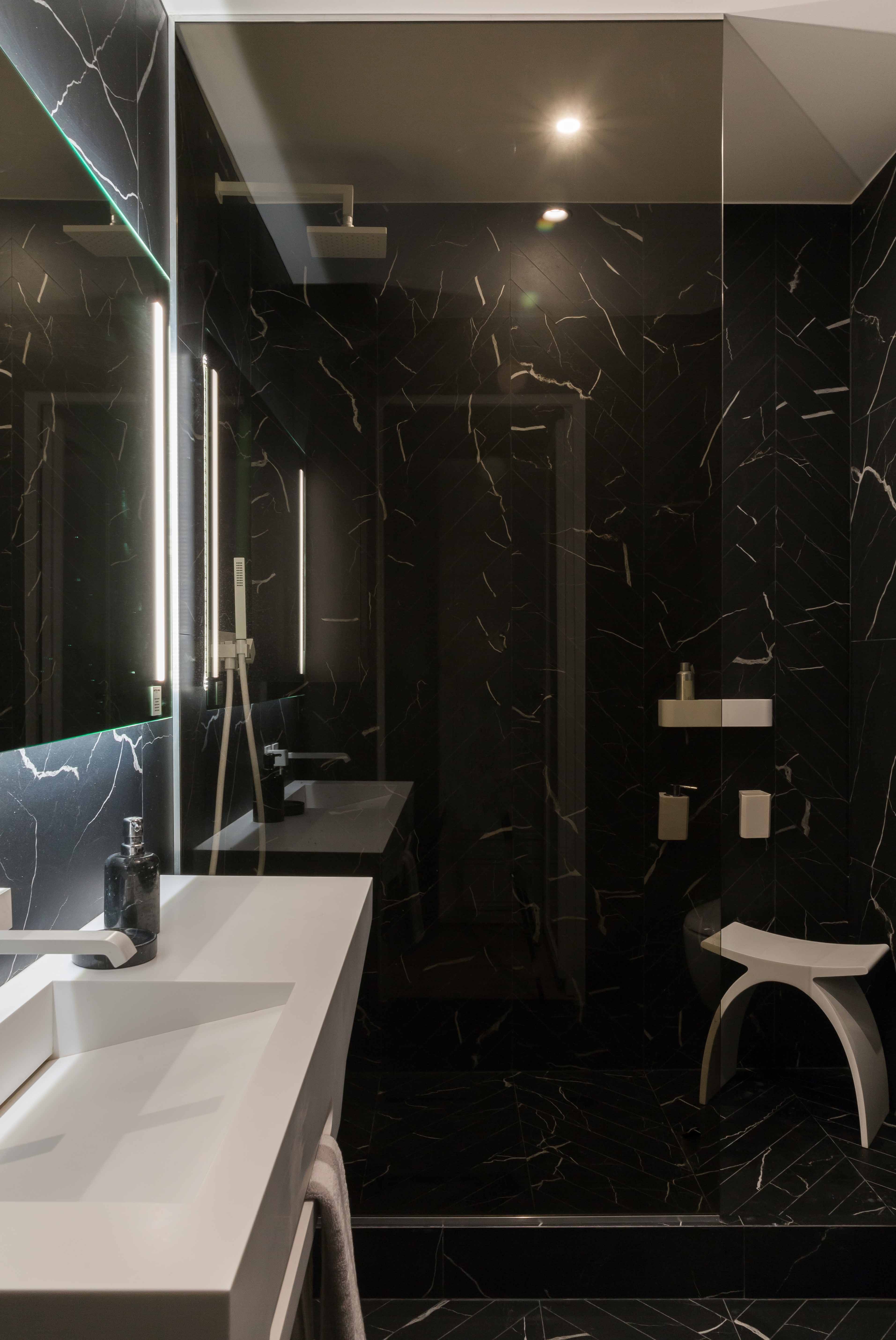 Salle d'eau en marbre sombre veiné, douche vitrée et plan-vasque clair monolithique