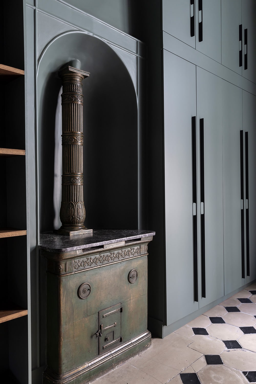 Poêle ancien en fonte patinée logé dans une niche cintrée, entre rangements sombres sur mesure