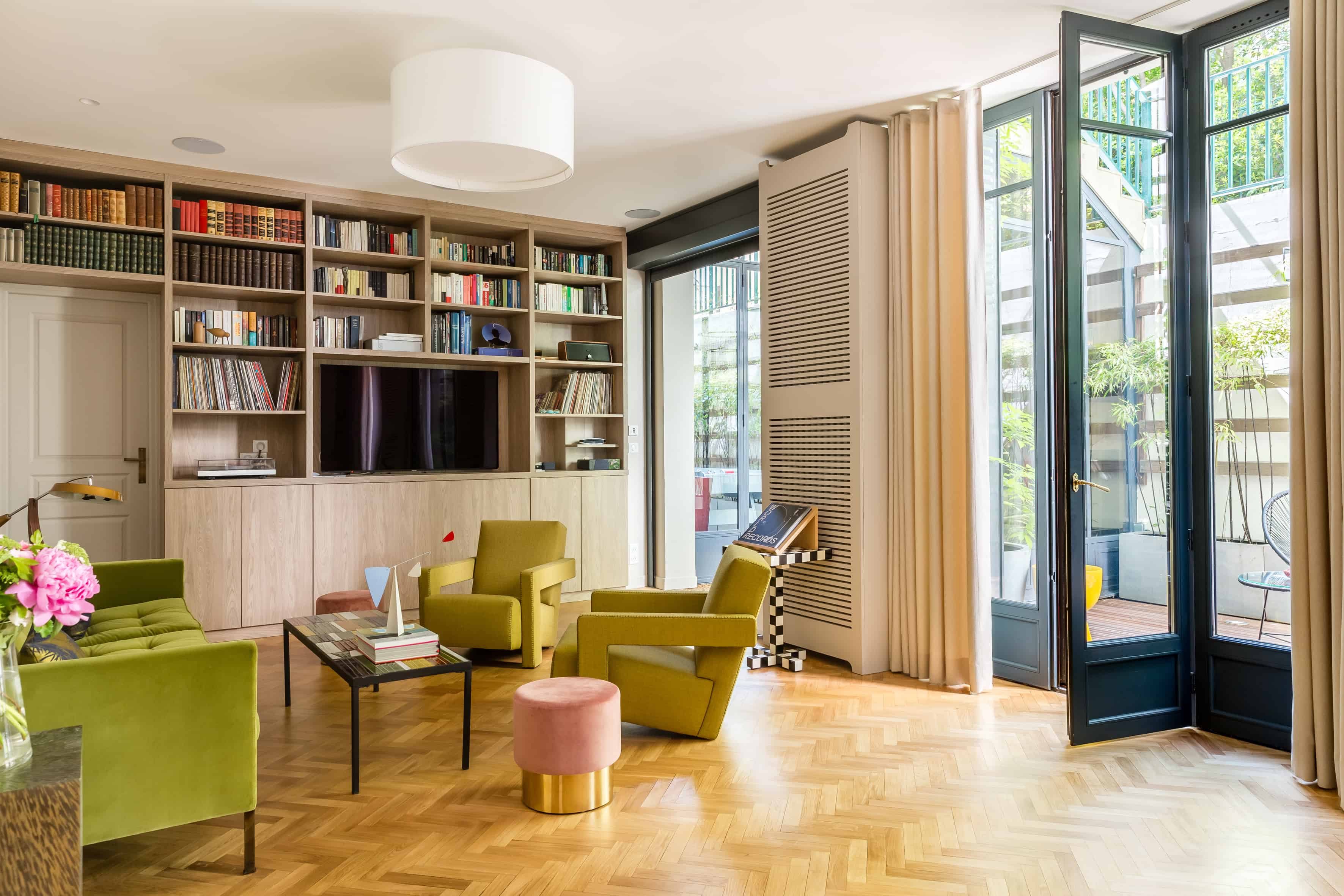 Bibliothèque intégrée toute hauteur et porte vitrée ouvrant sur la verrière et la cour plantée