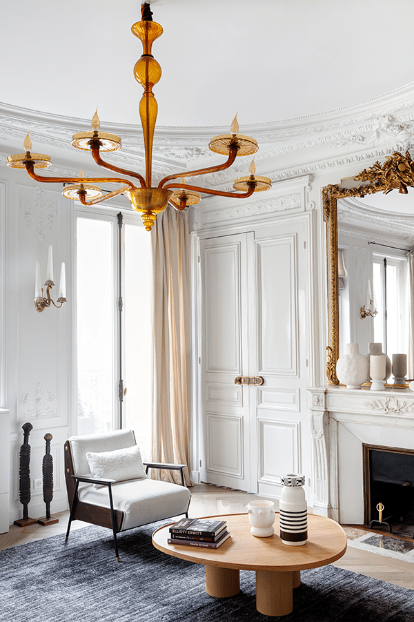 Salon clair sous lustre doré, fauteuil et table basse ronde devant la cheminée de marbre