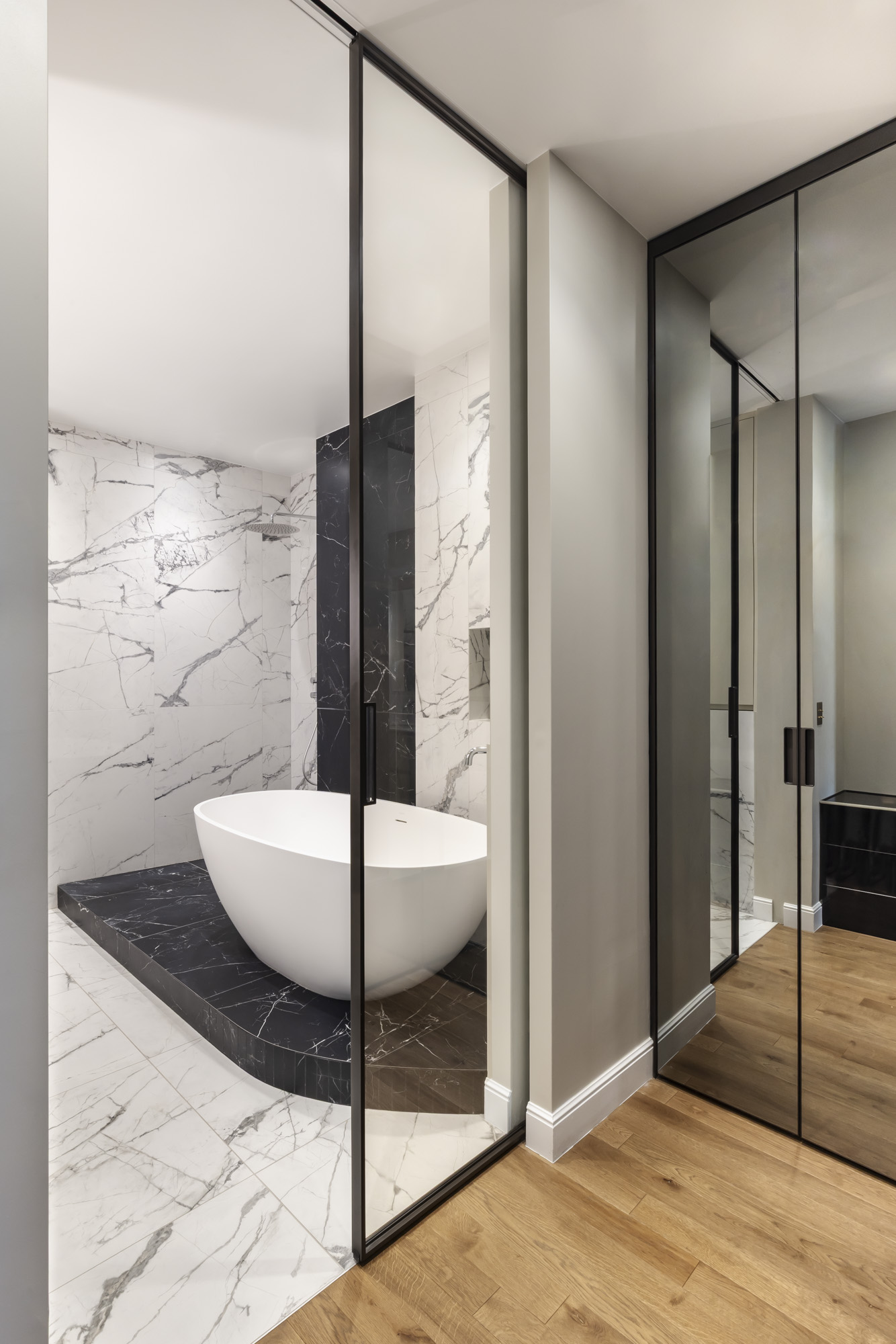 Salle de bain en marbre blanc et noir avec baignoire îlot et verrière