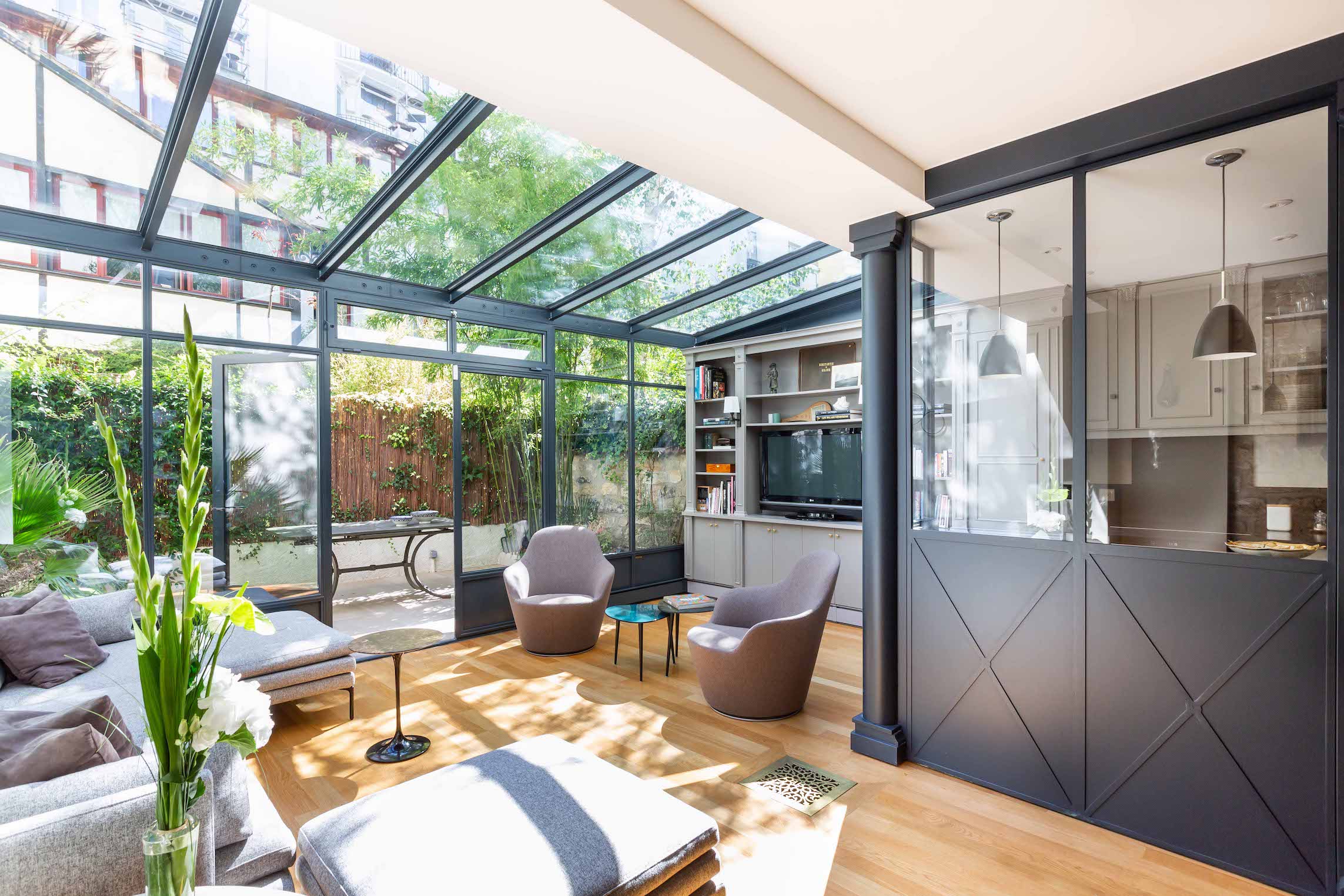 Séjour sous verrière avec fauteuils bas et menuiseries vitrées cadrant le jardin