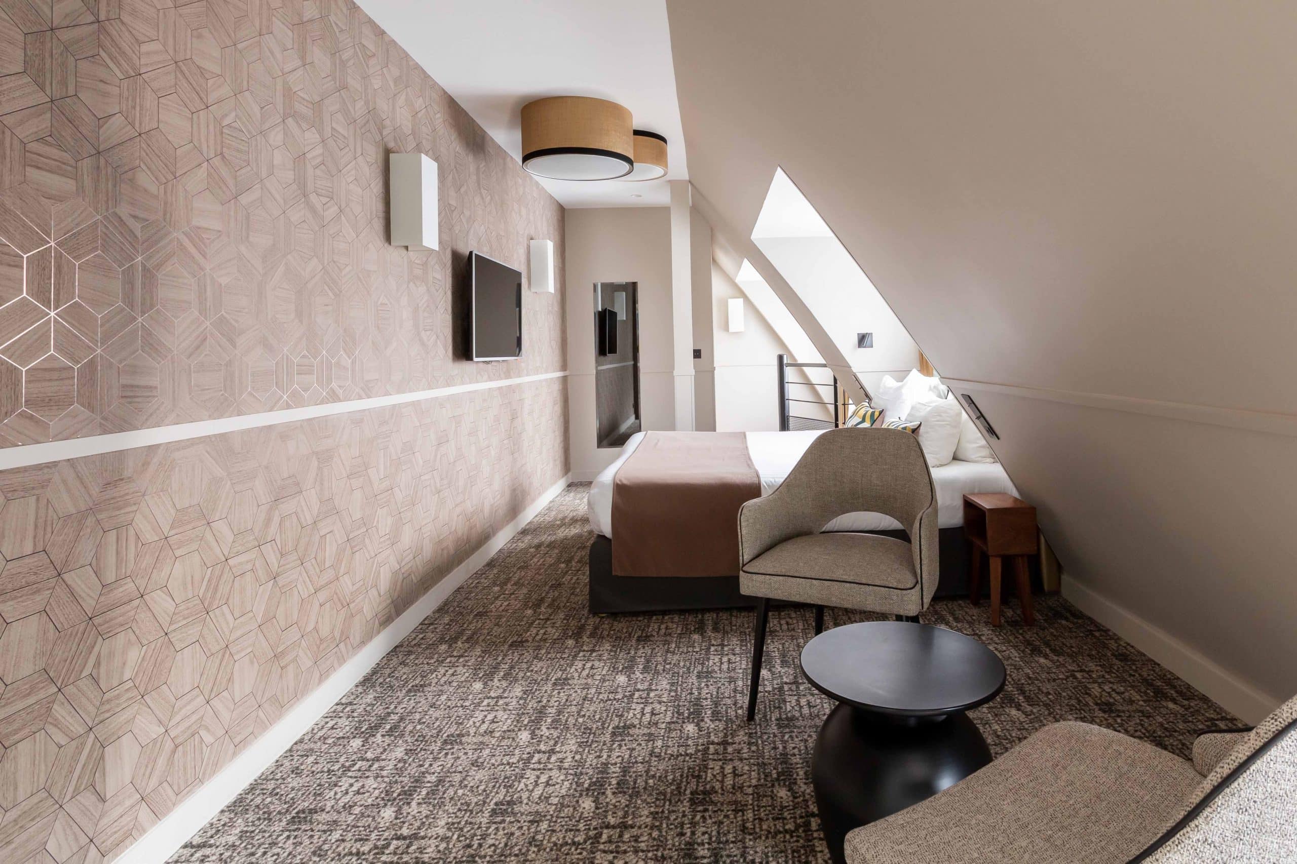 Chambre mansardée de l'Hôtel Daunou Opéra avec fauteuil et liseuse