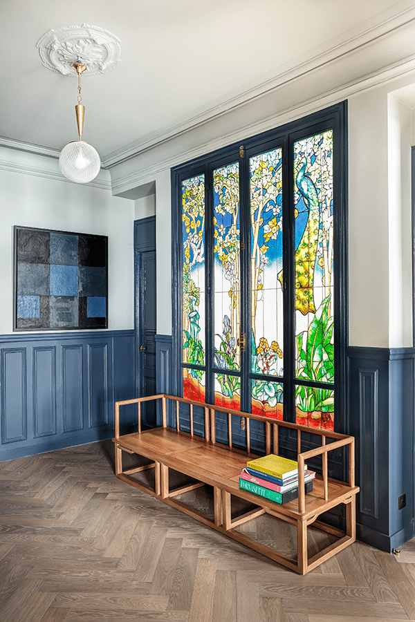 Pièce lambrissée bleue avec vitrail coloré et banc-bibliothèque en bois clair