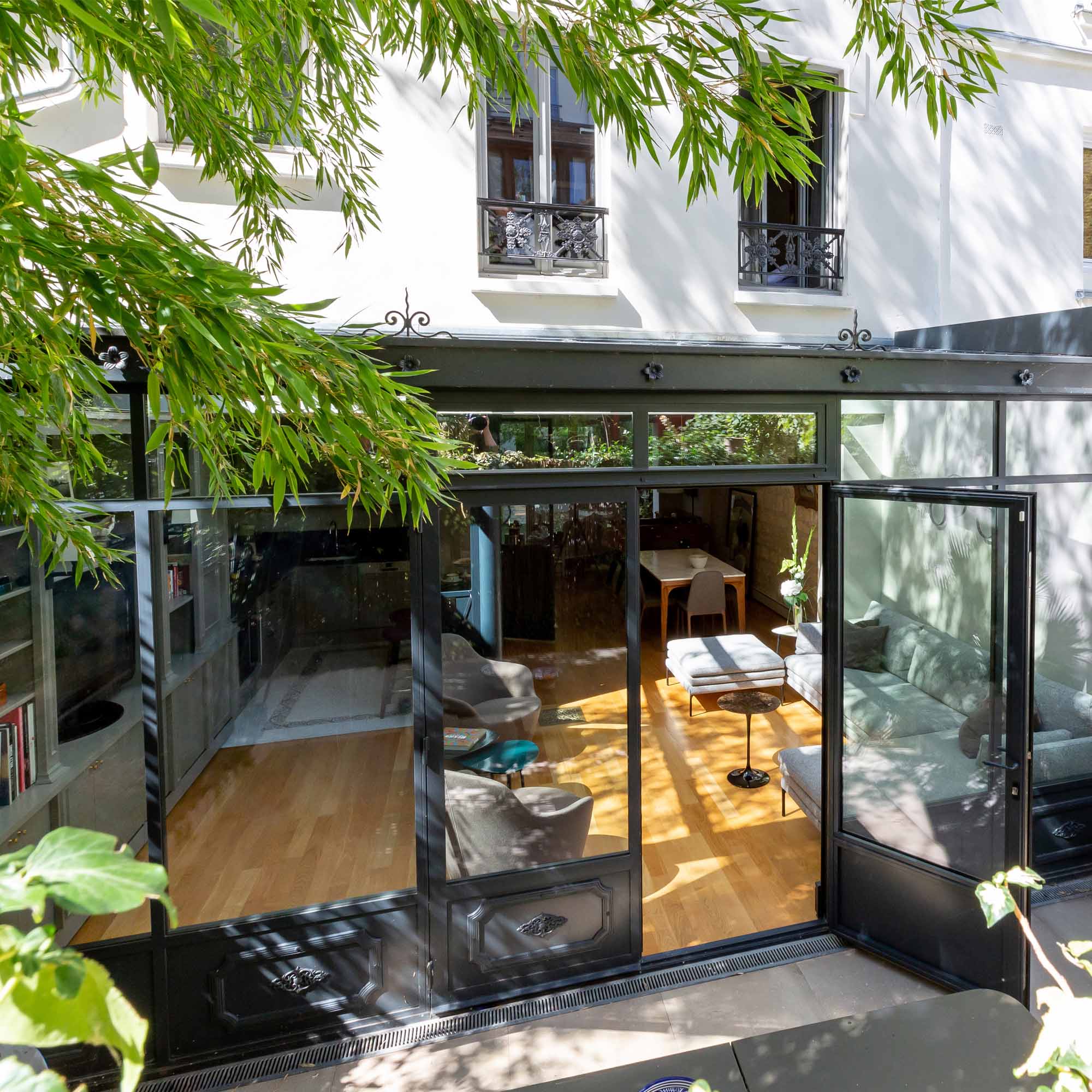 Extension vitrée de la maison vue depuis le jardin, à travers le feuillage