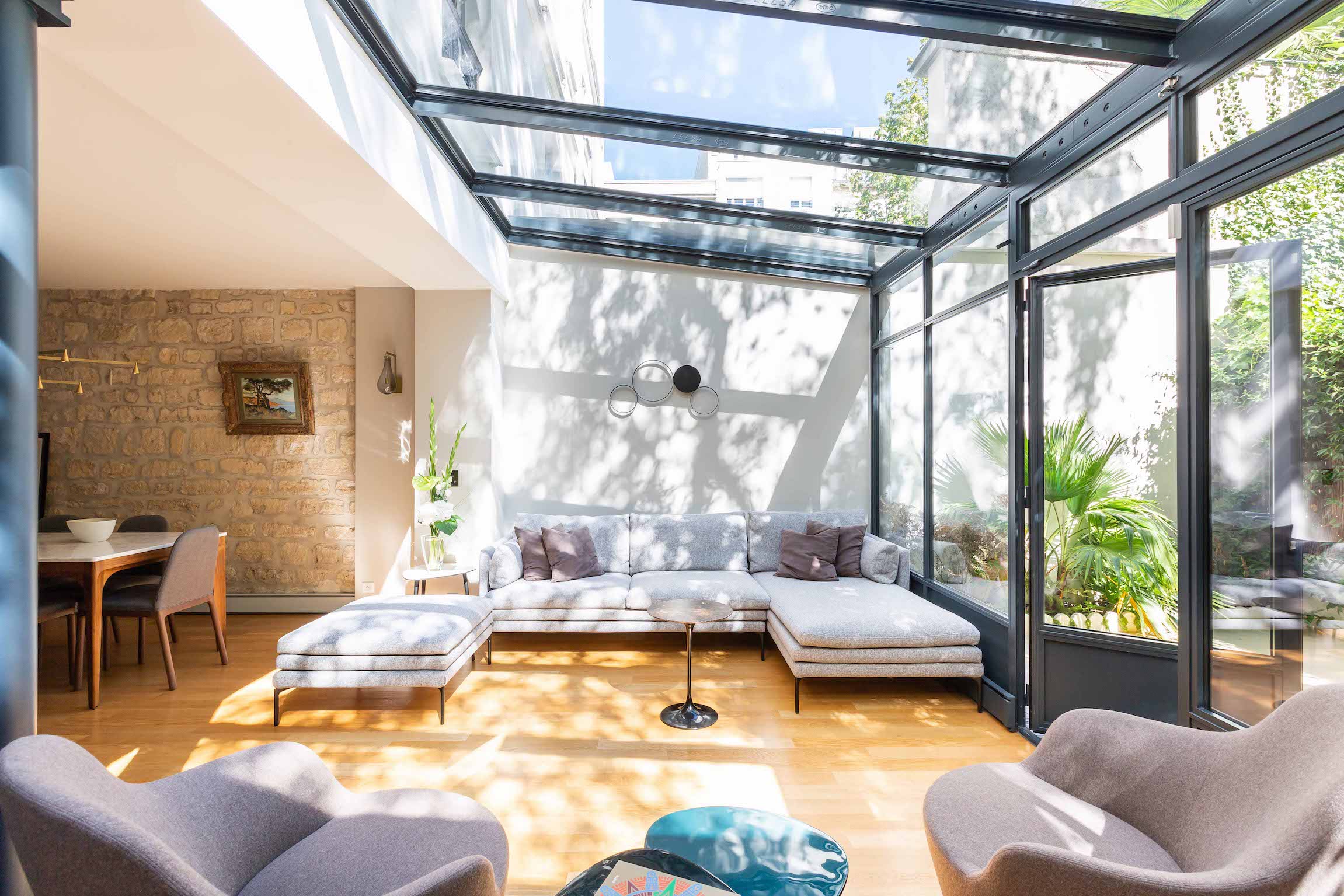 Pièce de vie sous verrière en acier, assises claires et coin repas, ouverte de plain-pied sur le jardin