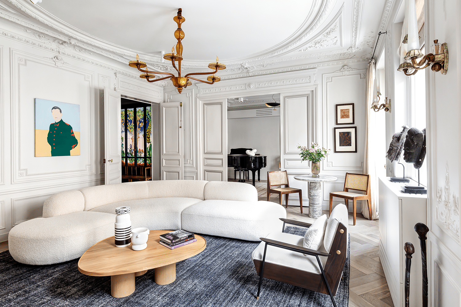 Salon parisien sous moulures et lustre doré, canapé courbe clair et cheminée en marbre blanc