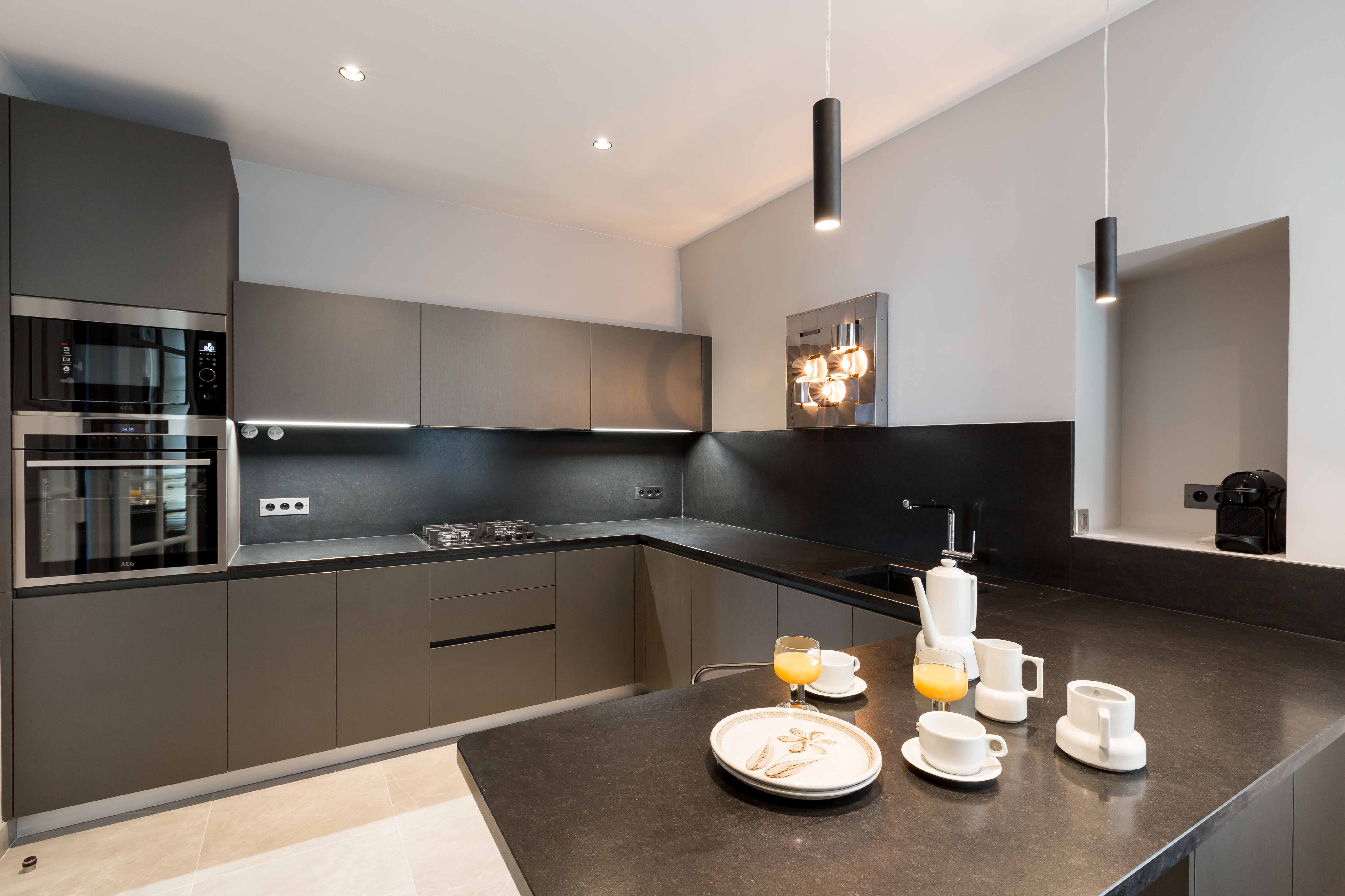 Cuisine contemporaine avec colonnes de four intégrées, plan de travail sombre continu et retour en table