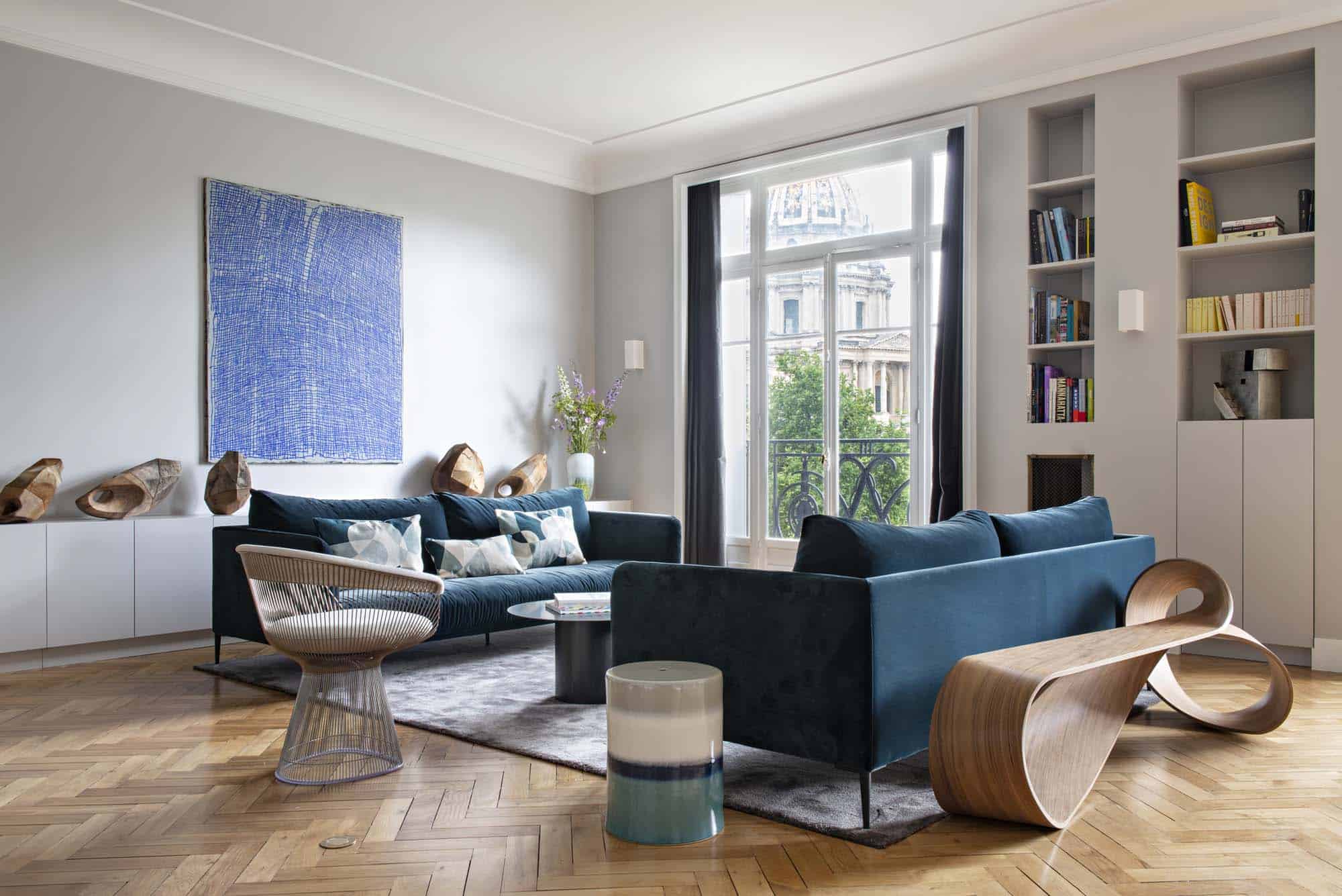 Salon avec canapés bleus, bibliothèque intégrée et grande fenêtre, parquet à point de Hongrie