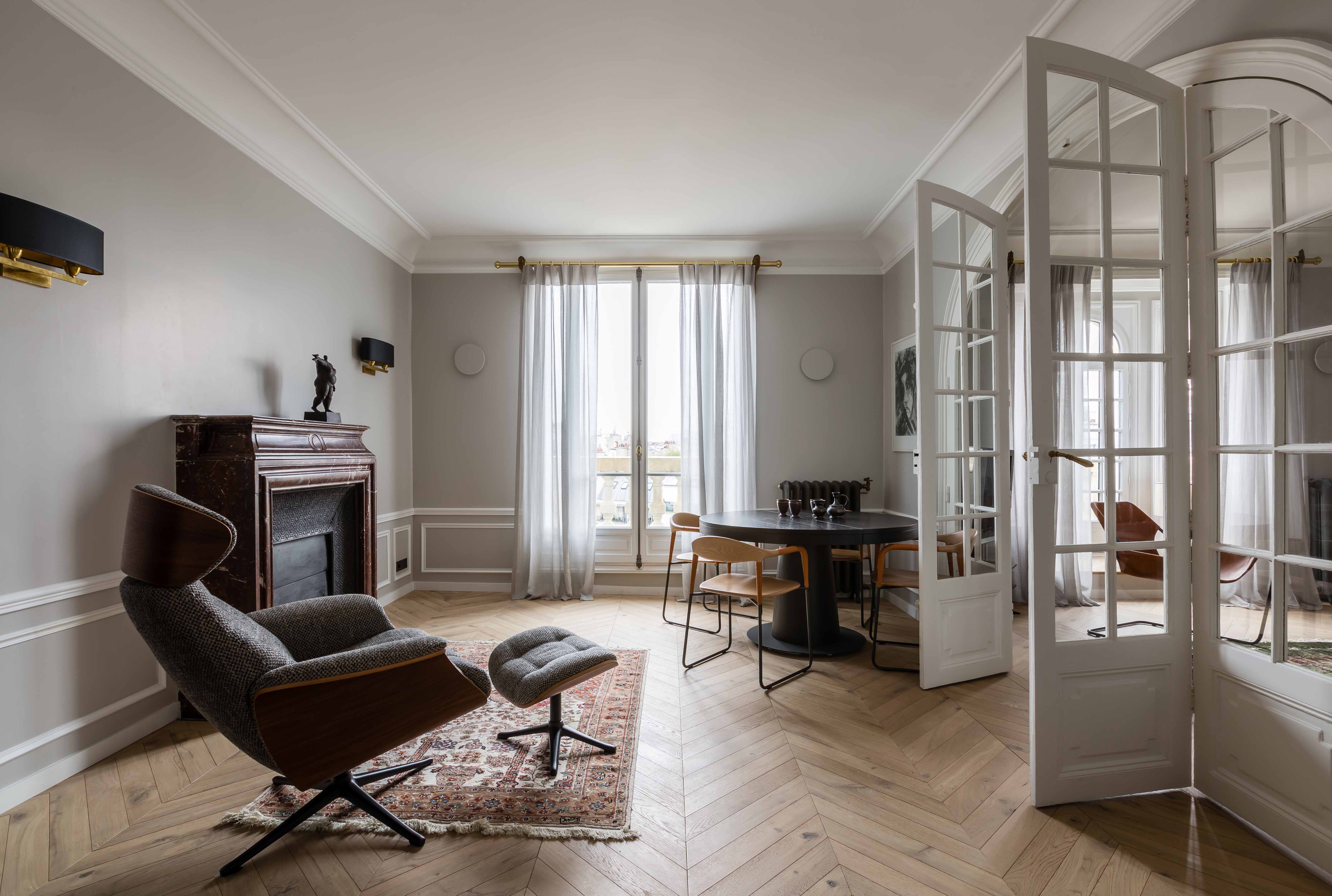Espace de réception avec cheminée, assise contemporaine et perspective vers la salle à manger par les portes vitrées
