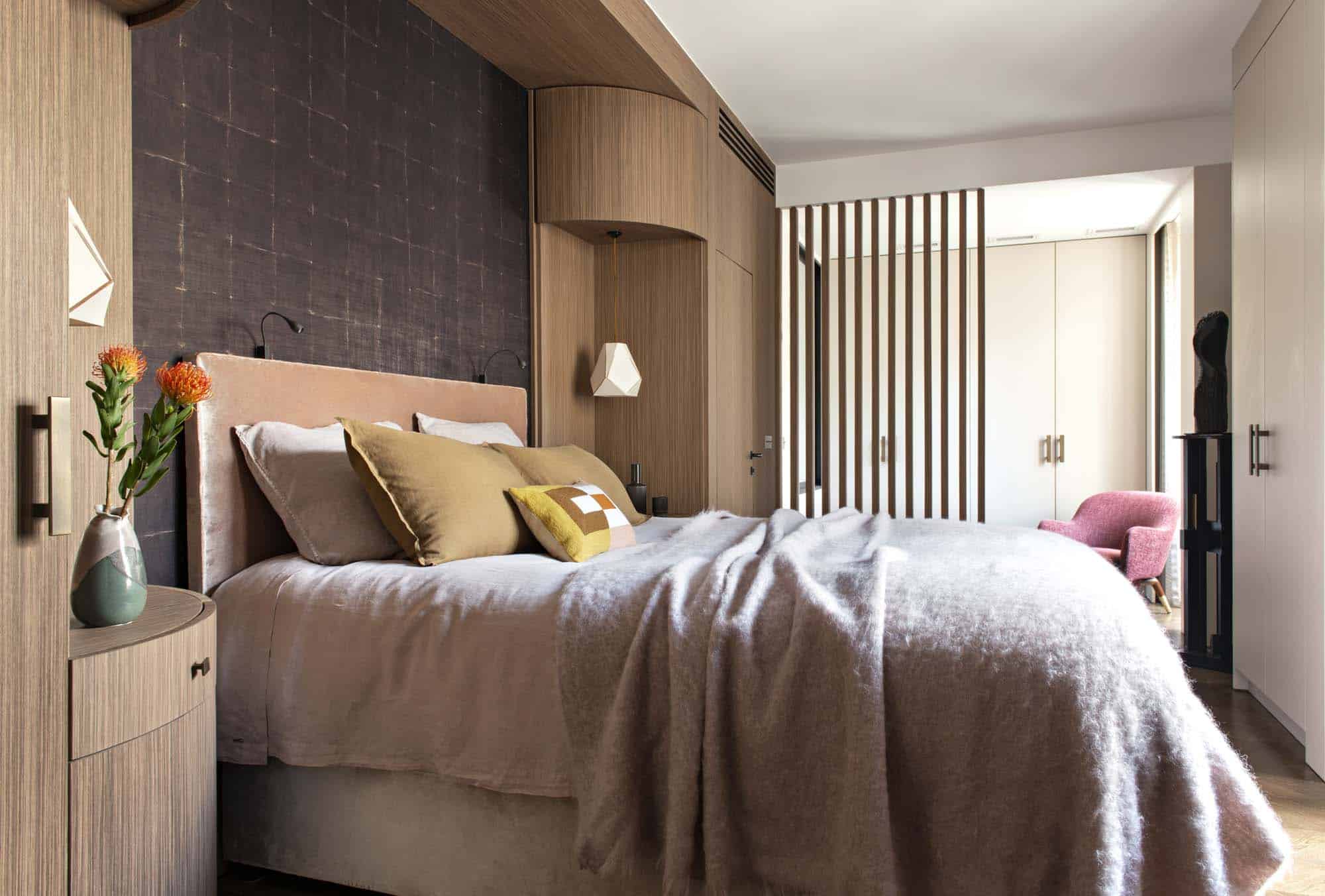 Chambre habillée d'une tête de lit murale texturée, menuiserie cintrée en bois clair et claustra vertical filtrant l'espace voisin