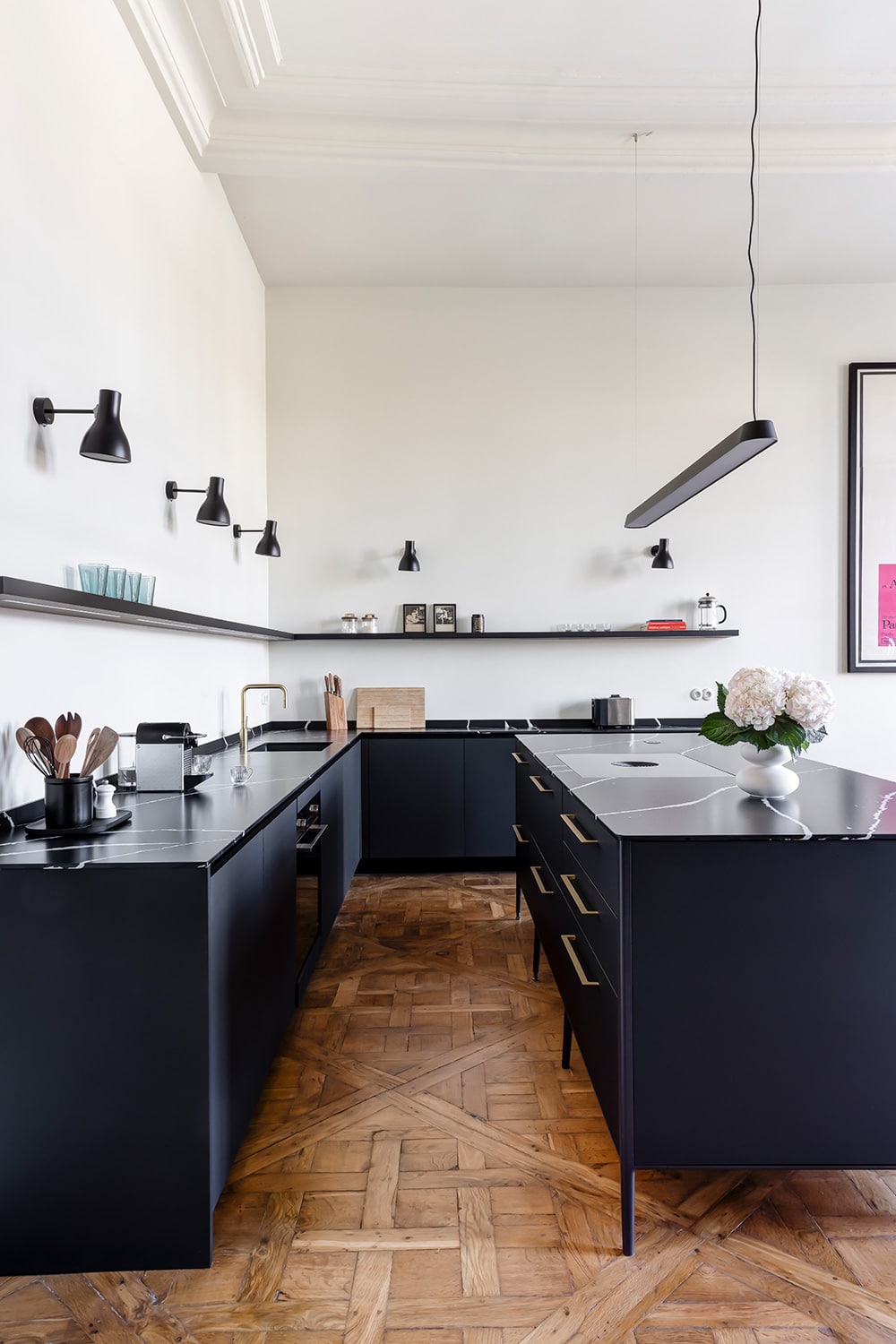 Cuisine linéaire aux façades noires sur parquet en point de Hongrie, plan continu et appliques d'atelier