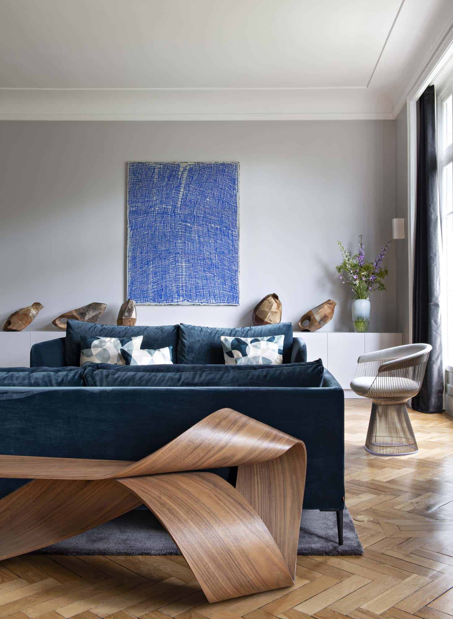 Canapé en velours bleu profond sous une œuvre encadrée, assise en métal et parquet à point de Hongrie