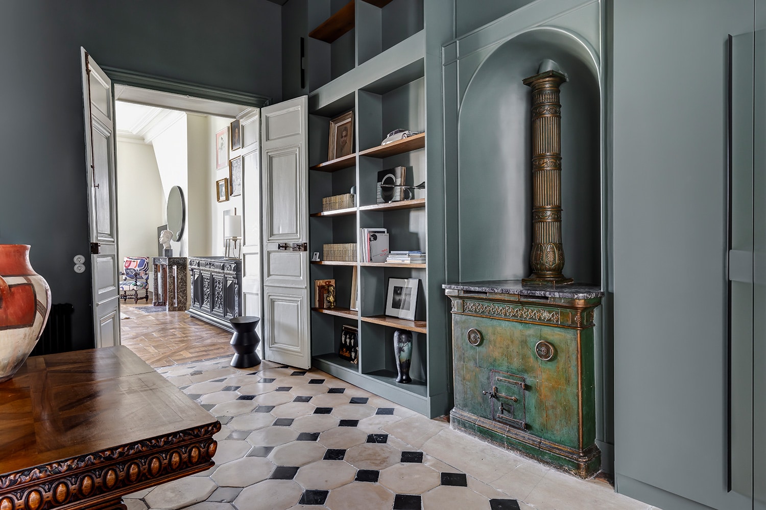 Enfilade cadrée par une porte double, bibliothèque sombre toute hauteur et sol en damier