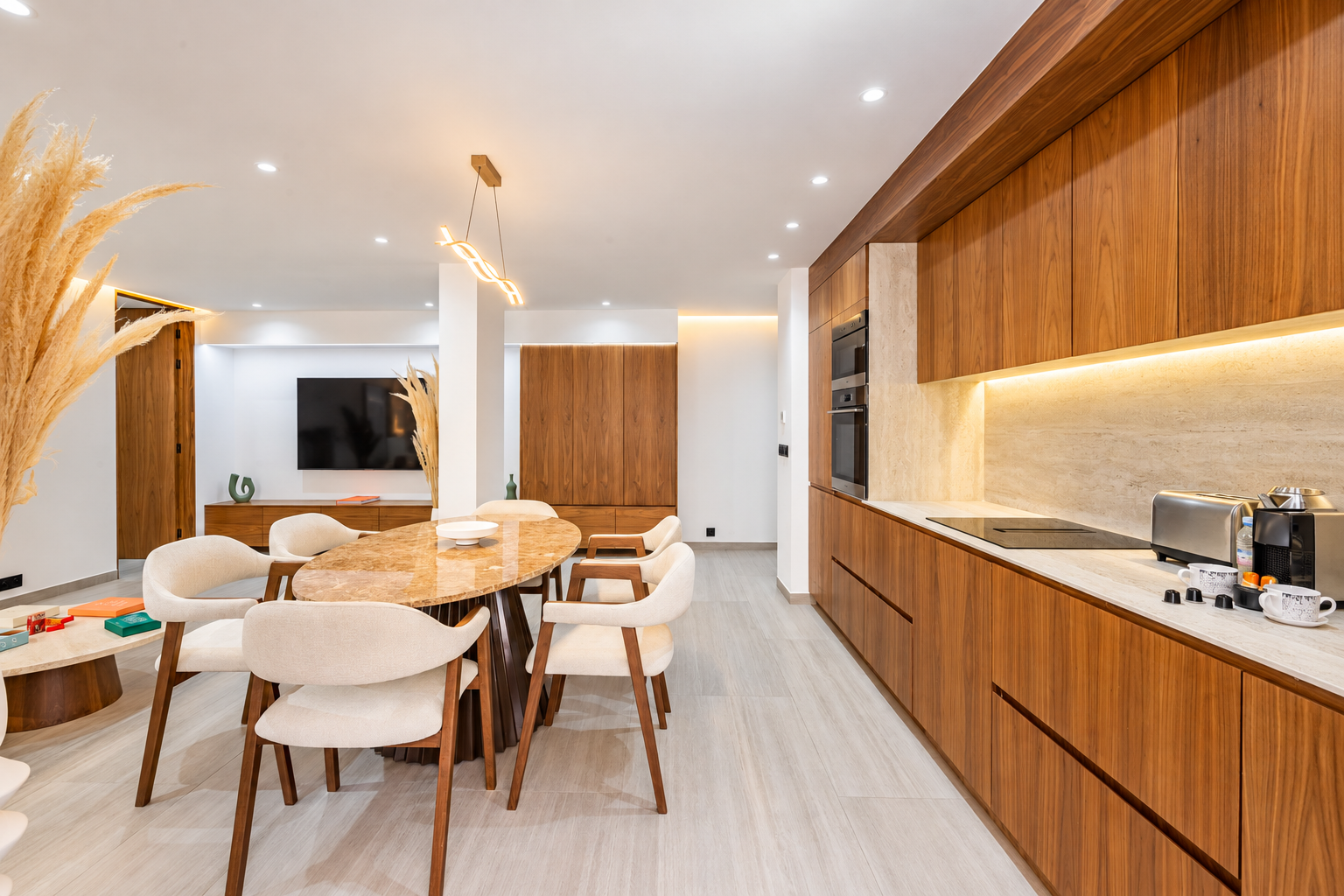 Salle à manger : table ovale en marbre, chaises gainées crème, cuisine ouverte en noyer et meuble TV