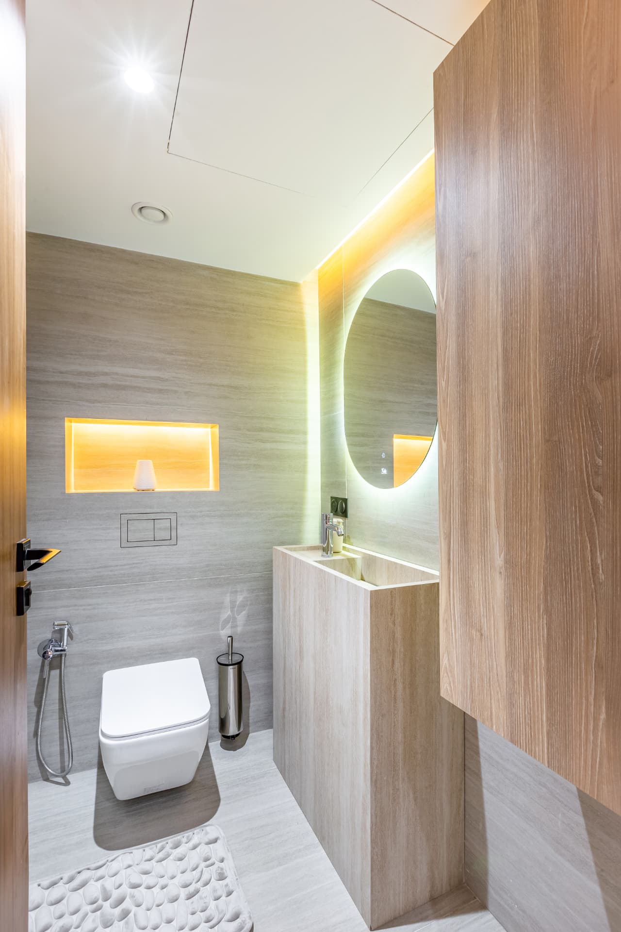 Toilettes invités : vasque en travertin, miroir ovale rétroéclairé et niche lumineuse