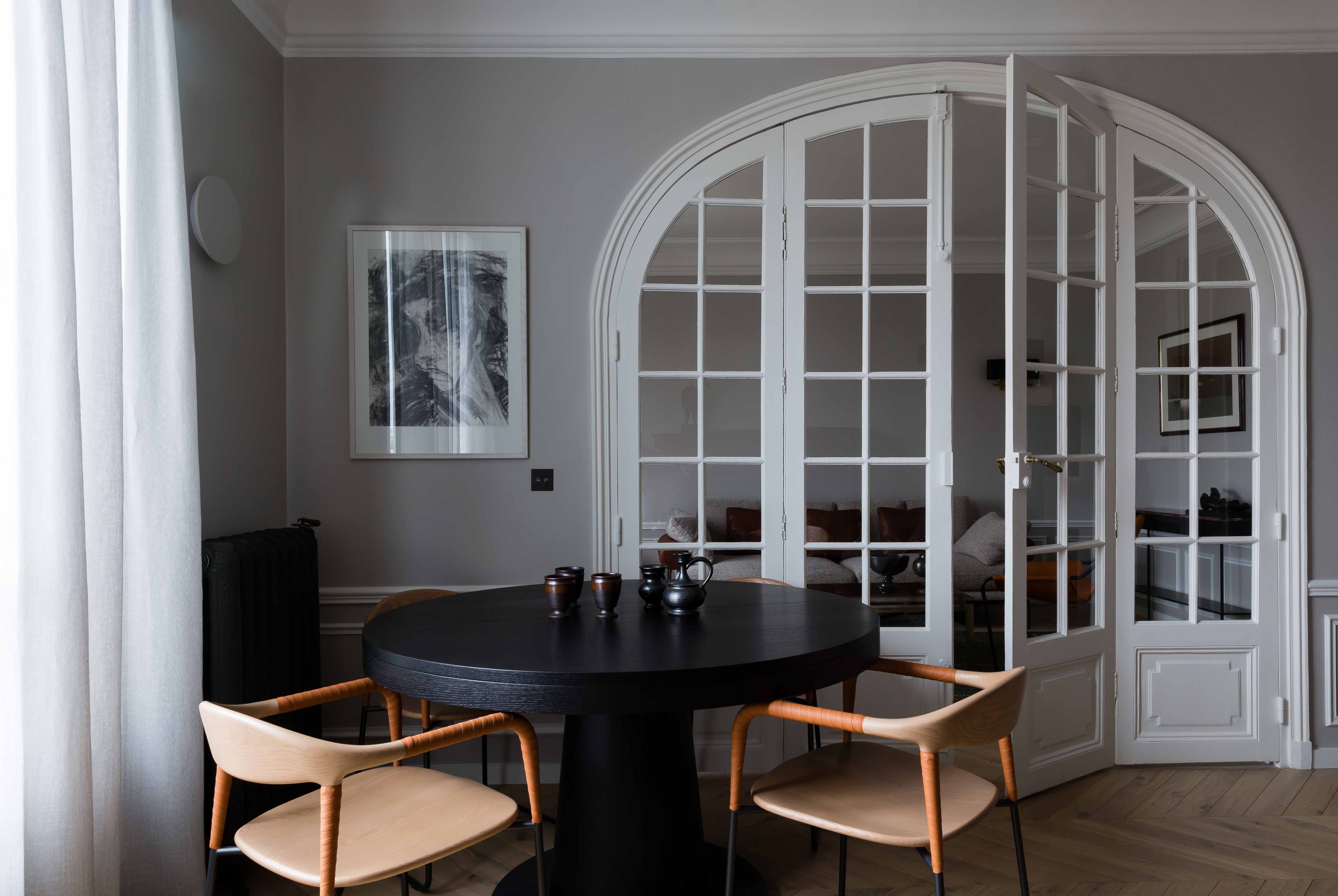 Salle à manger avec table ronde sombre devant l'ensemble de portes vitrées cintrées
