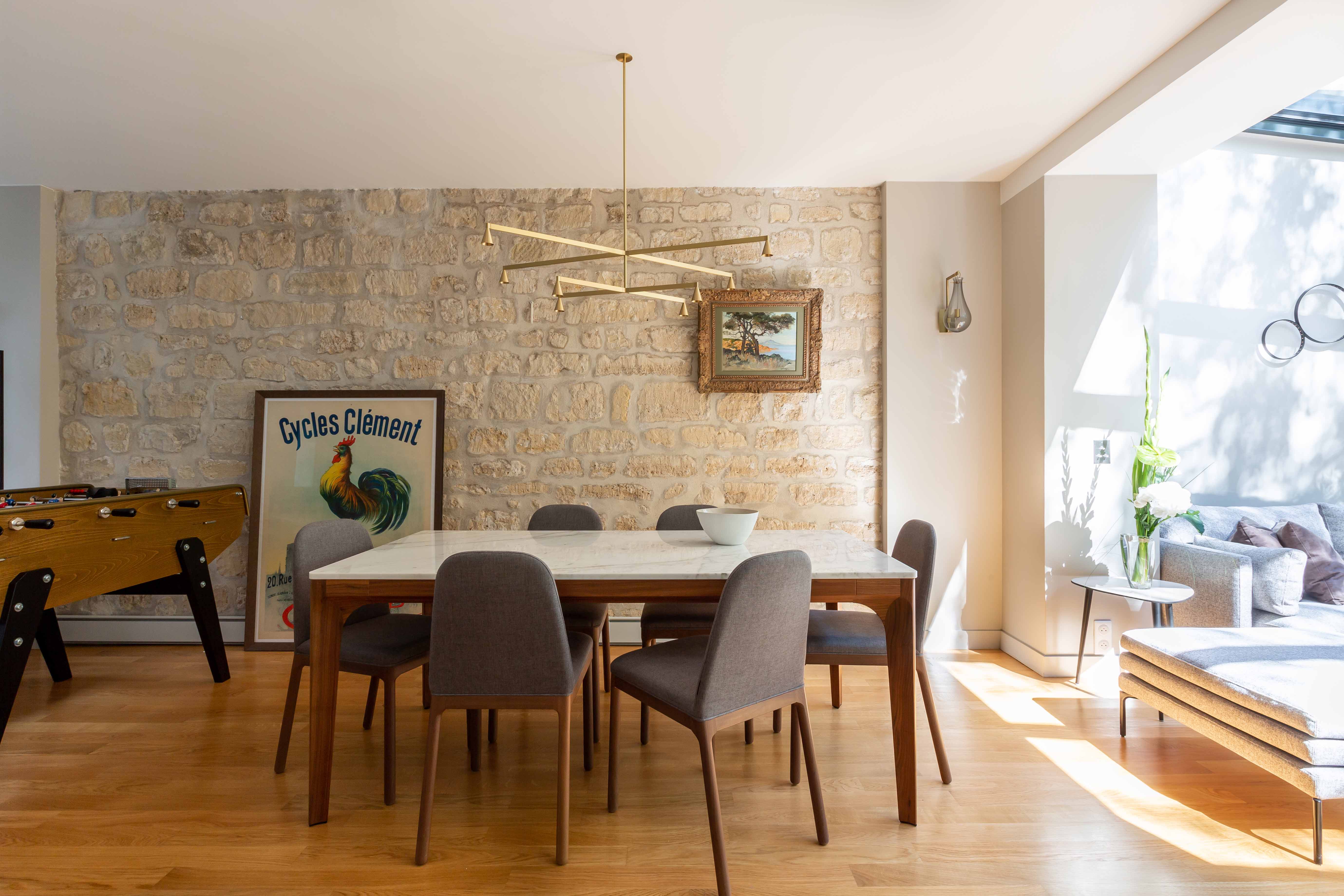 Salle à manger devant un mur de pierre apparente, longue table et suspension linéaire