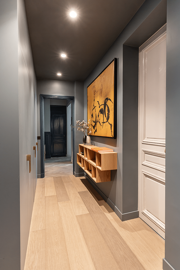 Couloir aux murs sombres, éclairage encastré et parquet clair menant aux pièces privatives