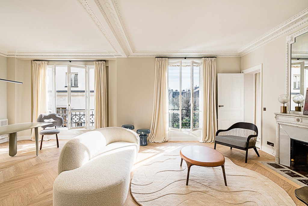 Salon lumineux d'un appartement haussmannien, canapé courbe et parquet en point de Hongrie